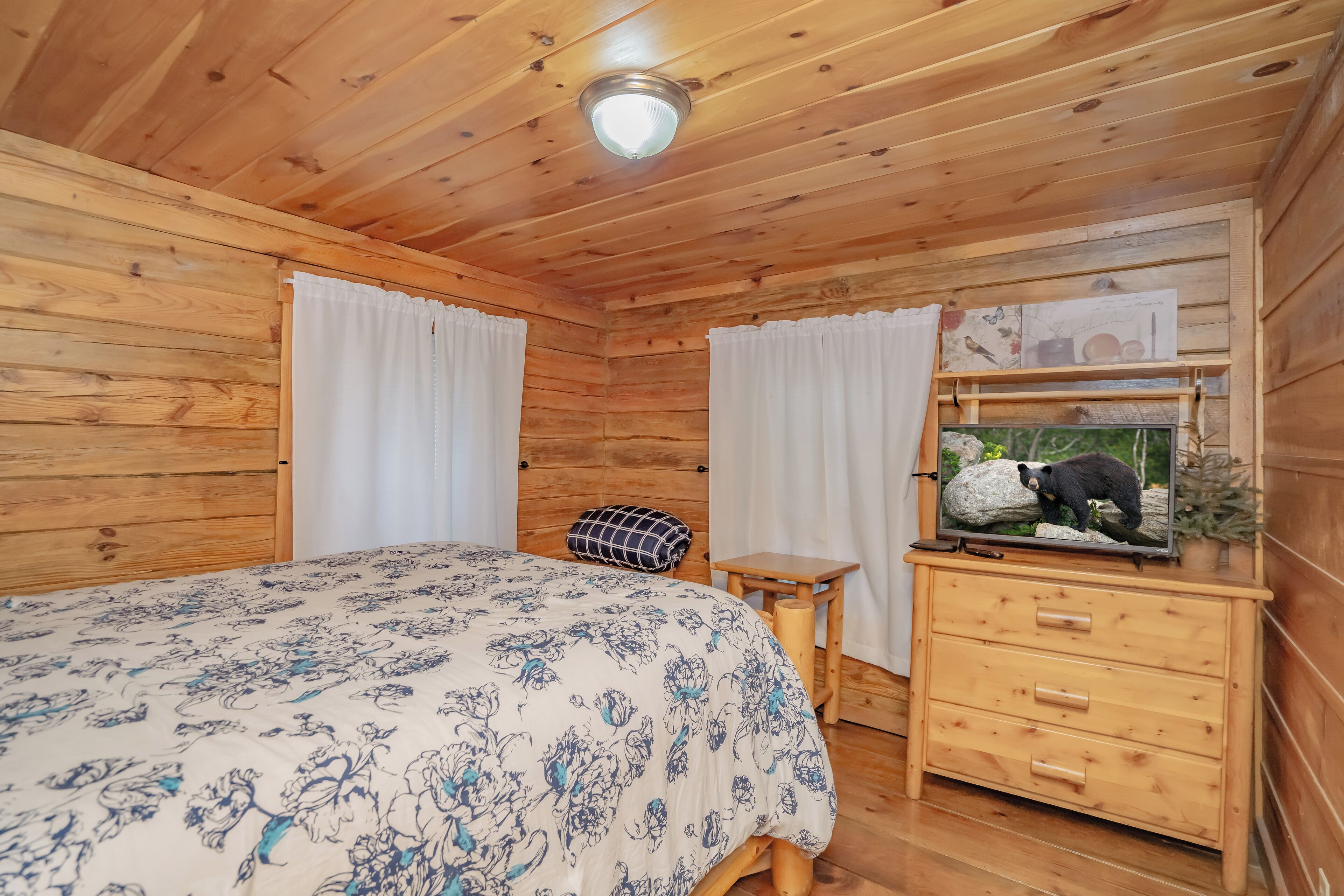 A wooden cabin room with a bed, a dresser, and a television on the dresser.
