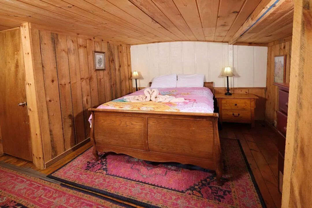 A wooden-paneled room with a bed, two bedside tables with lamps, and a door.