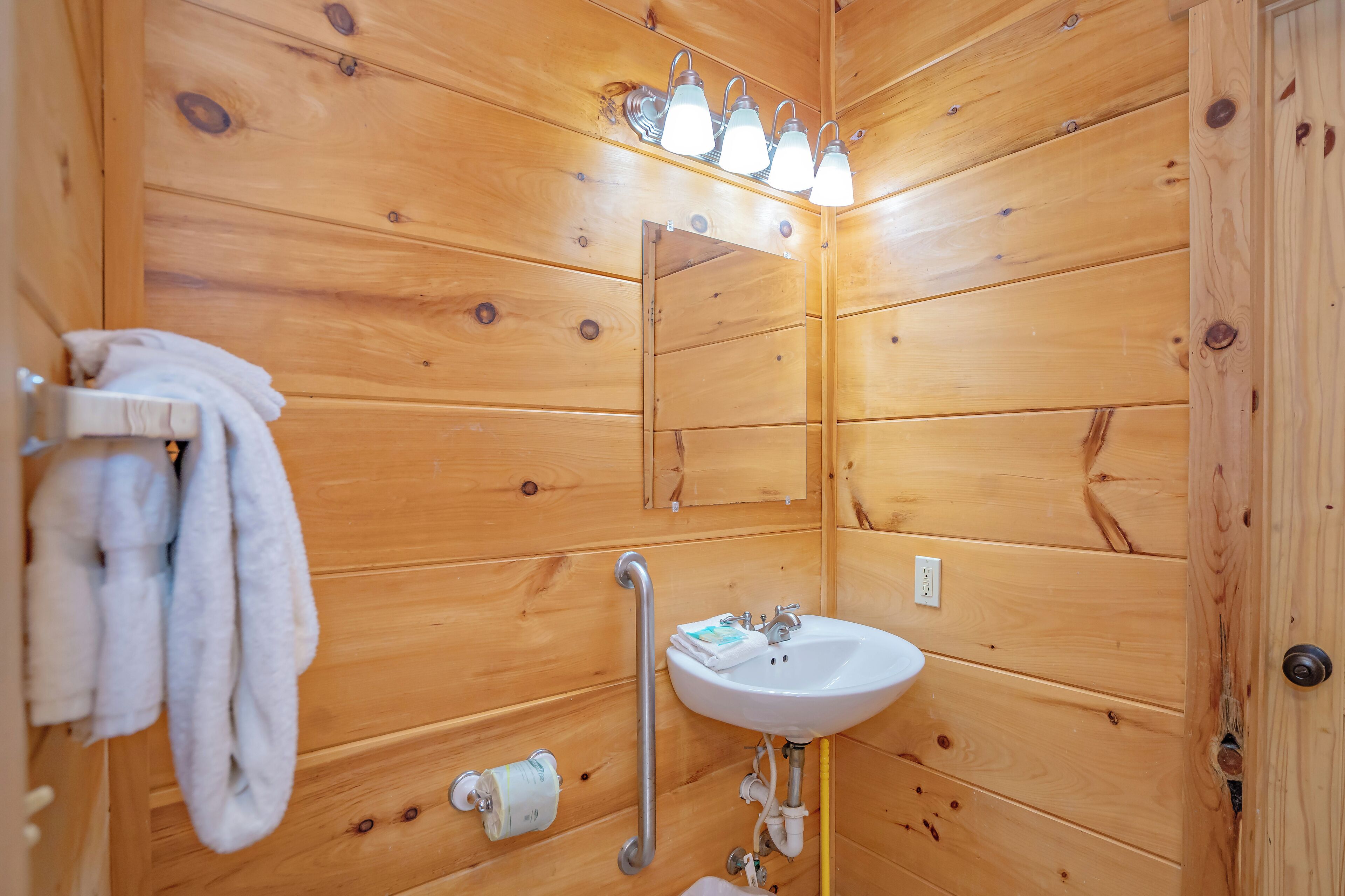 A wooden bathroom with a sink, mirror, towel rack, and a grab bar.