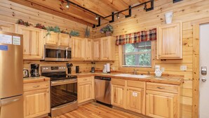 Une cuisine avec des meubles en bois, des appareils électroménagers en acier inoxydable et une fenêtre équipée de stores.