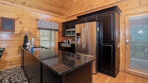 A modern kitchen with wooden walls, a granite countertop, stainless steel appliances, and a black cabinet. - 🌳 Keaton's Cozy Cabin 🌲 Wooded Retreat, Resort Pool & Hot Tub (Sevierville)