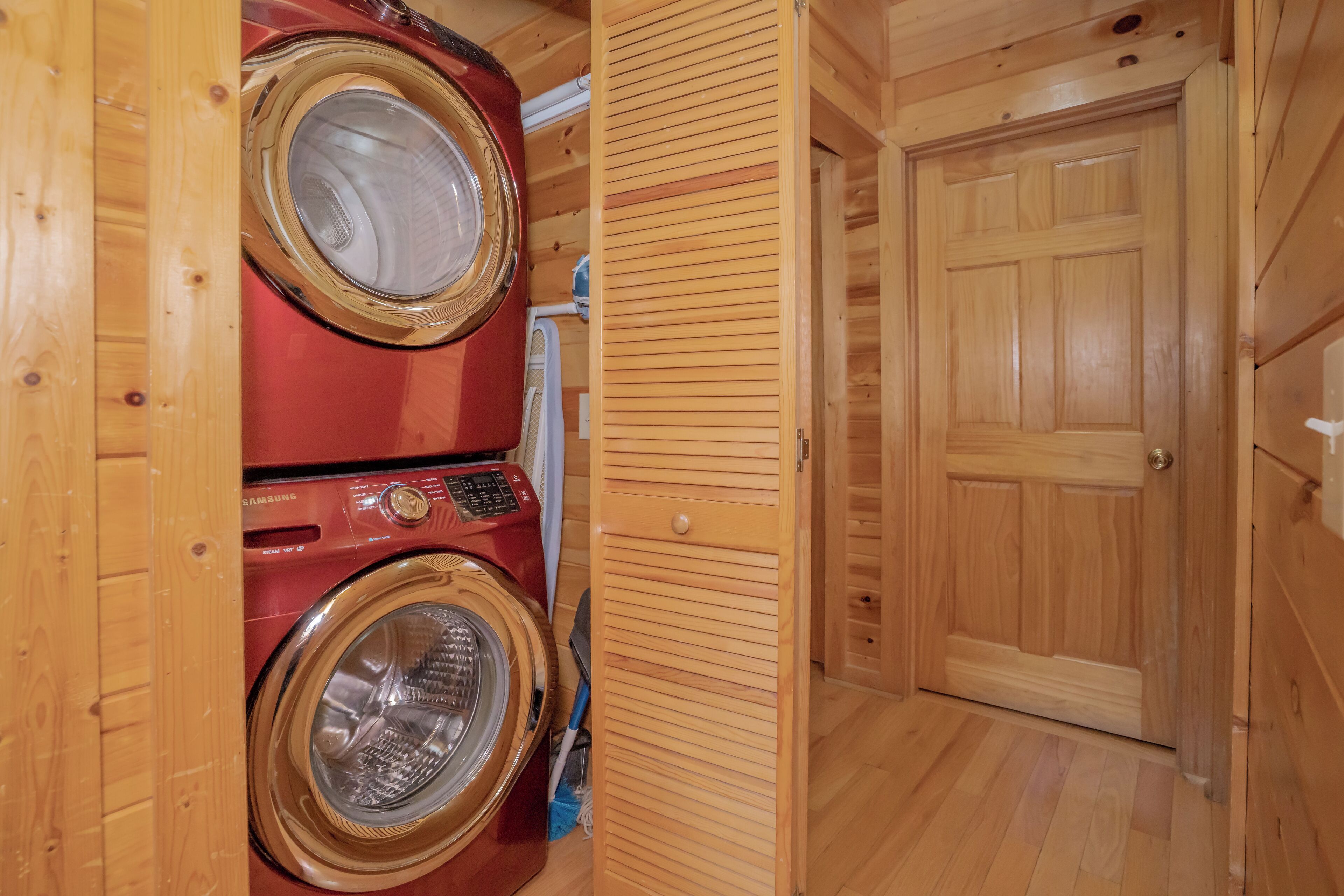 A laundry area with two stacked washing machines, a wooden door, and a wooden floor.