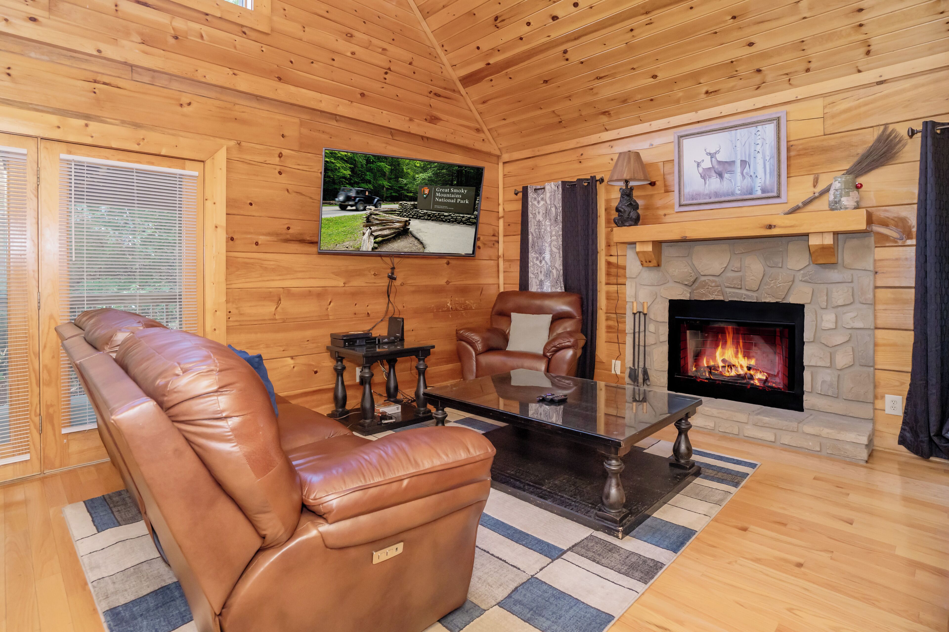 A cozy living room with a leather sofa, a fireplace, a television mounted on the wall, and a stone fireplace surround.