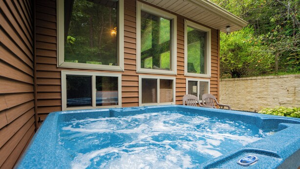 A hot tub in front of a wooden house with large windows and a stone wall. - Keaton's Firefly Meadow: OutdoorPool*HotTub*Games*Wifi*FirePit*Yard*Large Groups (Sevierville)