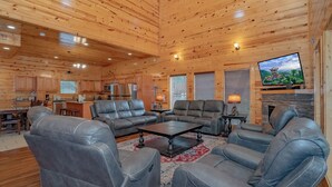 Amplia sala de estar con sofás de cuero y chimenea, paredes de madera y una zona de cocina.