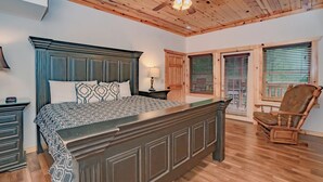 Un dormitorio con una cama grande, techo de madera y una silla junto a la ventana.