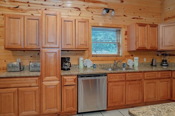 A kitchen with wooden cabinets, a dishwasher, a granite countertop, and a window with blinds.