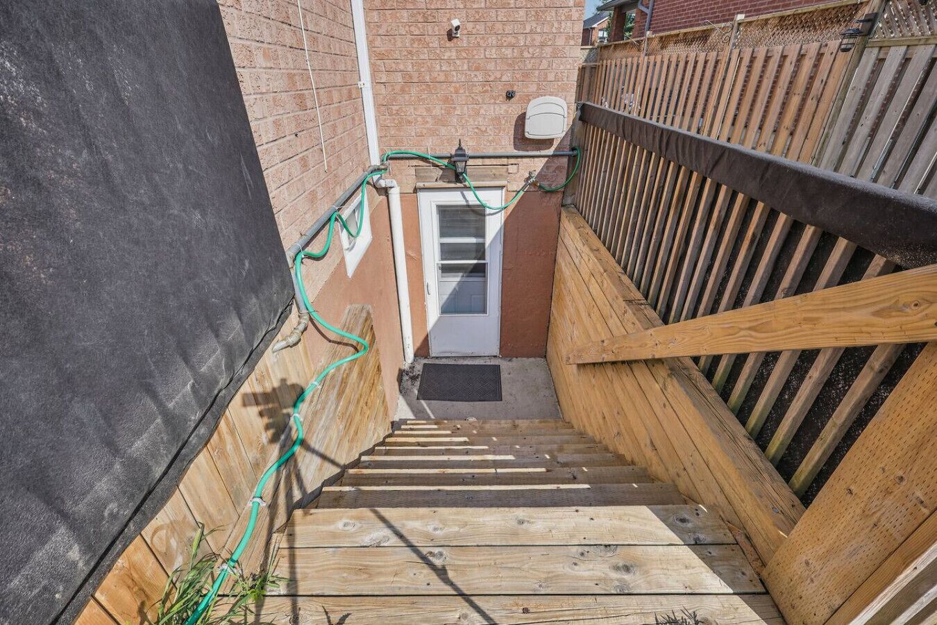 A narrow wooden staircase leading to a door, surrounded by a brick wall and a wooden fence.