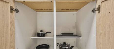 A kitchen cabinet with two shelves, each holding cookware.