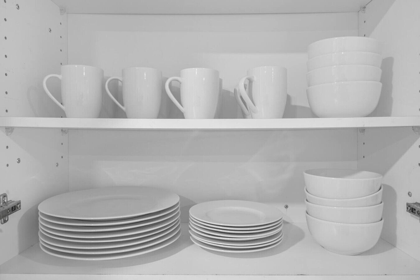 A white shelf with white mugs, bowls, and stacked plates.