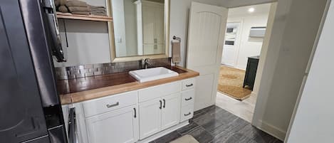 A modern kitchen with a stainless steel refrigerator, white cabinetry, a wooden countertop, and a large mirror above the sink.