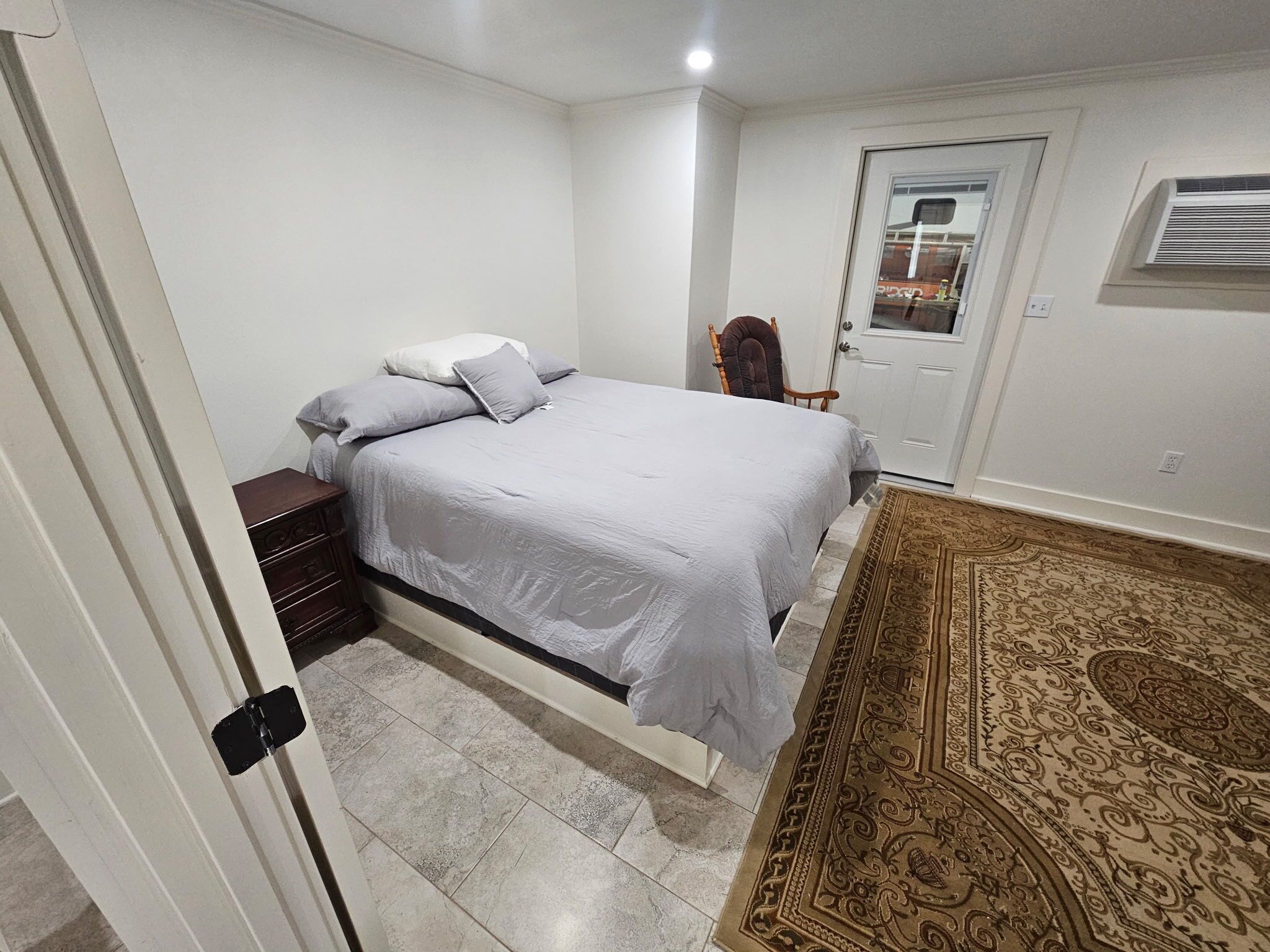Une chambre à coucher avec un lit, une chaise, une porte et un tapis à motifs.