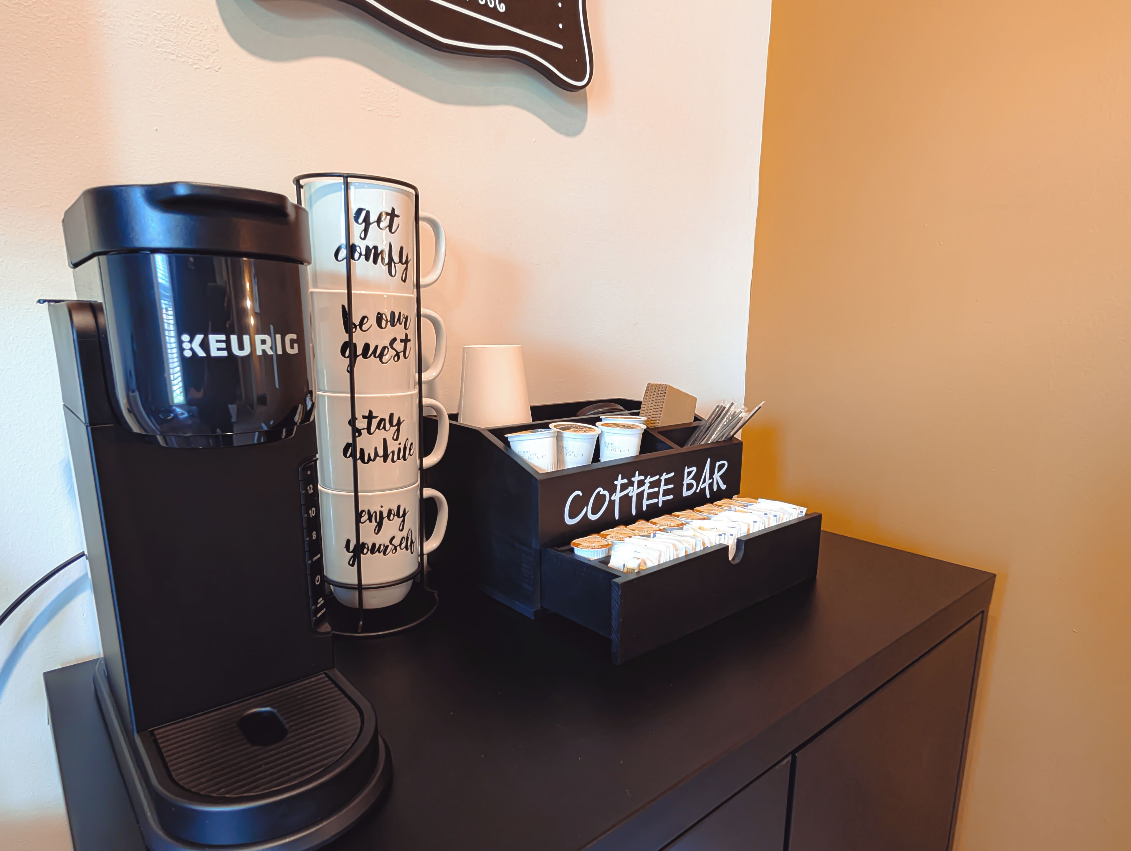 A coffee station with a Keurig coffee maker, a mug with motivational phrases, and a coffee bar with various items.