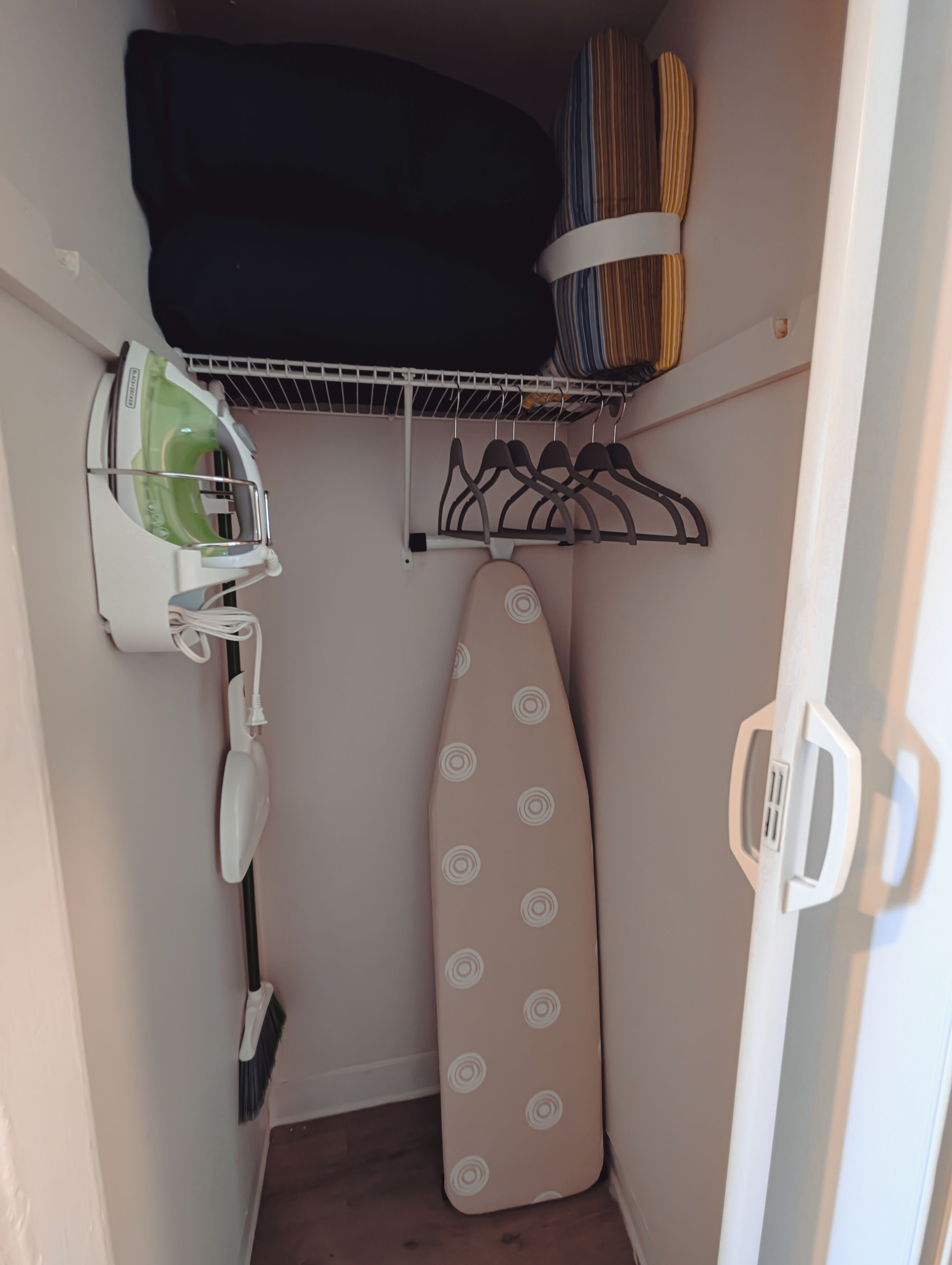 A compact storage area with a hanging rack, an ironing board, and a broom.