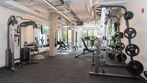 A modern gym with various exercise equipment, large windows, and a spacious layout.