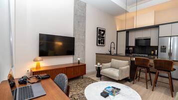 A modern living room with a flat-screen TV, a wooden coffee table, a sofa, and a dining area with two chairs.