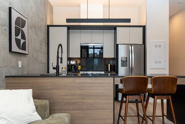 Uma cozinha moderna com uma ilha central, eletrodomésticos de aço inoxidável e um espaço de bar com dois bancos.