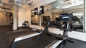 Une salle de sport équipée de machines de cardio, dotée d’un mur avec des miroirs et d’un grand écran de télévision.