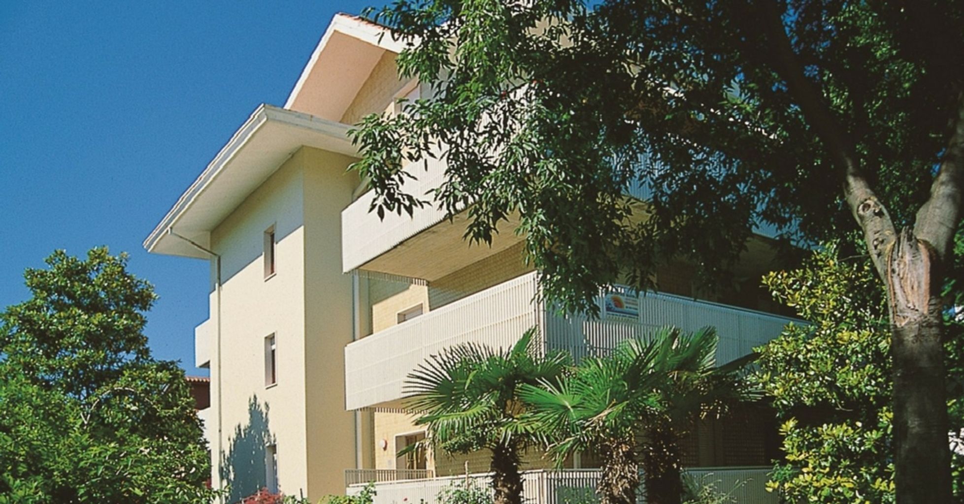 Un edificio de varios pisos con techo plano, rodeado de árboles y vegetación.