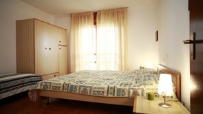 A bedroom with a bed, a wardrobe, a bedside table with a lamp, and a window with curtains.