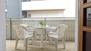 A round table with four chairs, a potted plant, and a glass of water on a balcony with a white railing.
