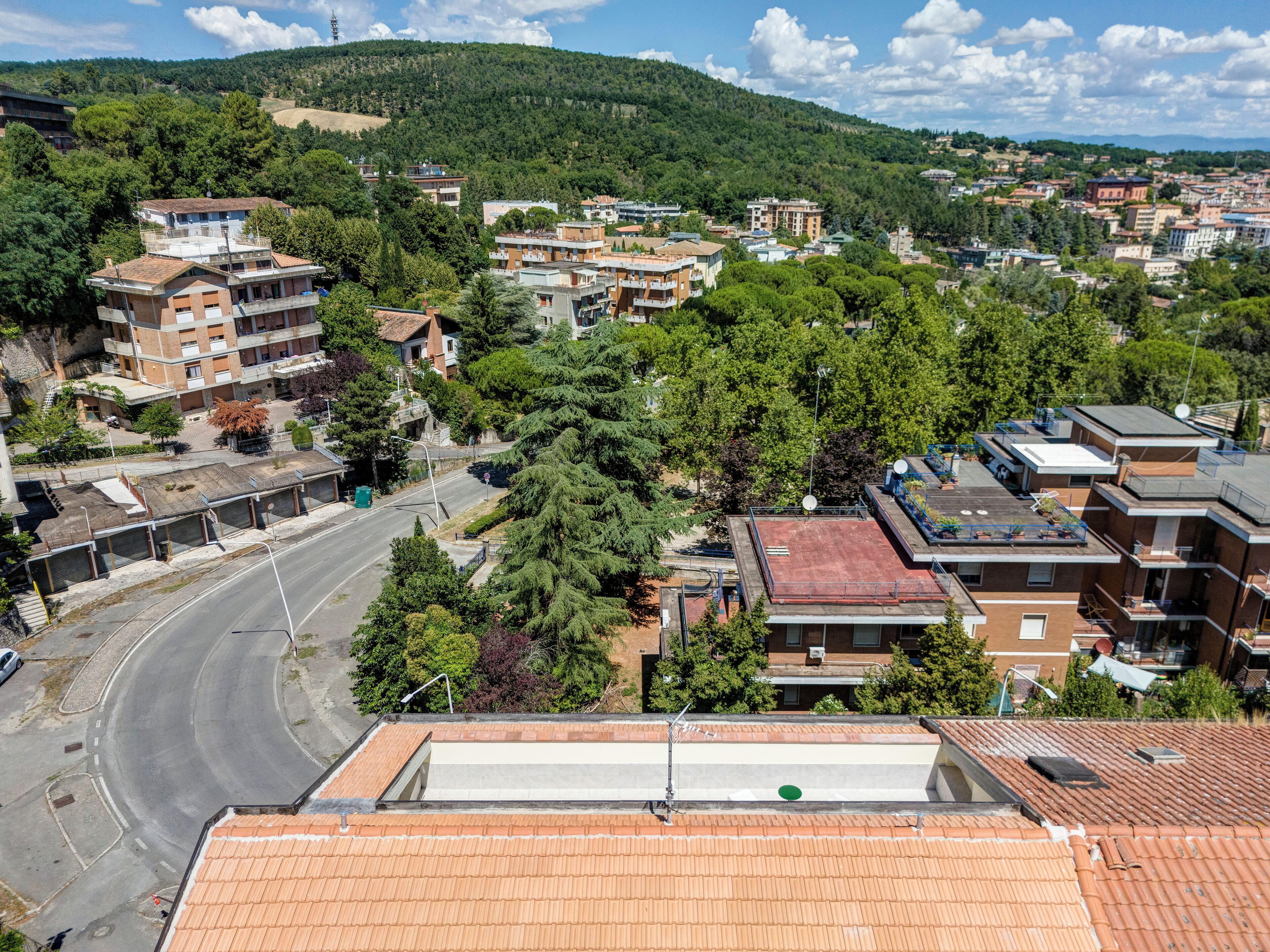 Zona residencial con varios edificios, una carretera sinuosa y un paisaje montañoso al fondo.