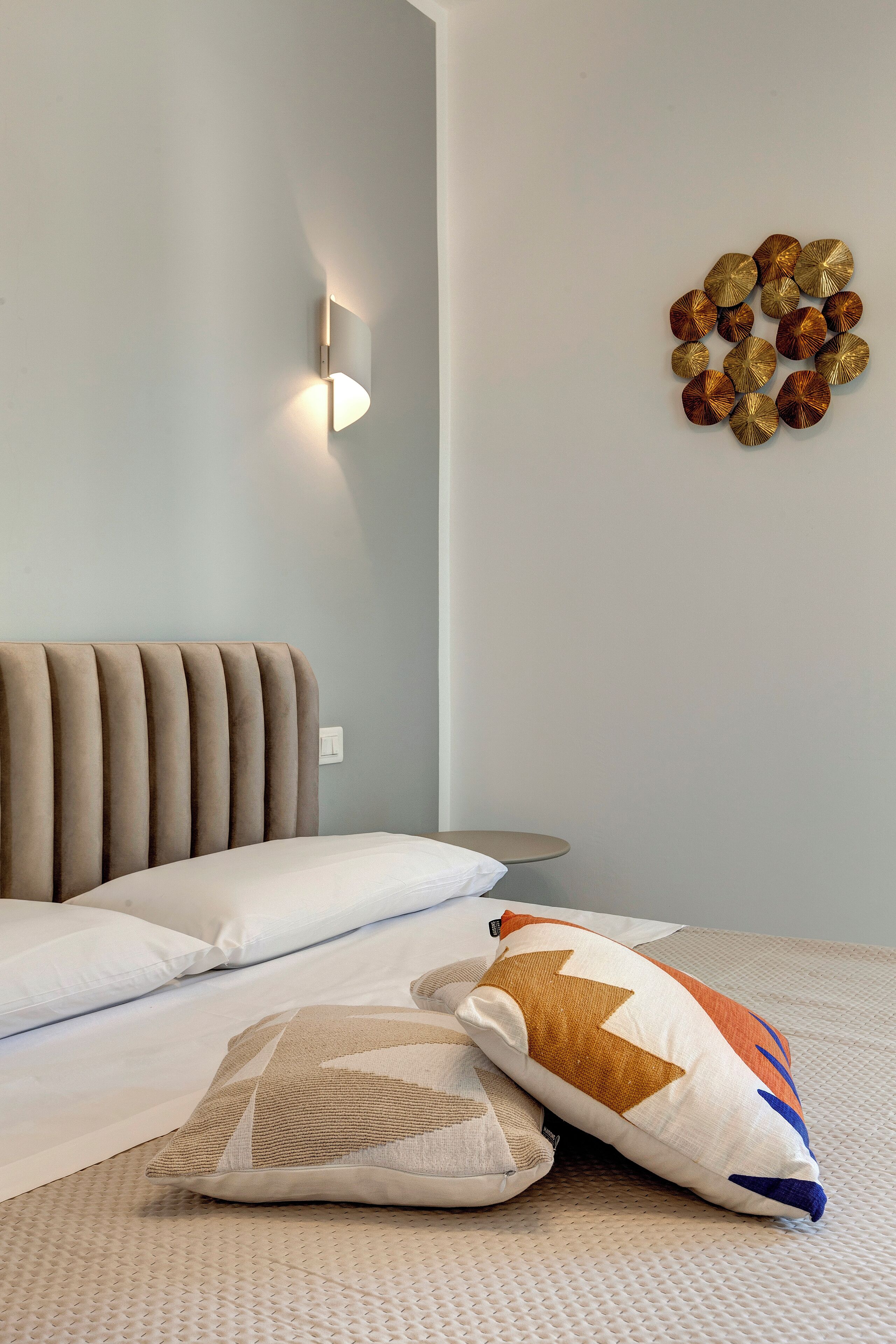 A bedroom with a bed, pillows, a wall-mounted light, and a decorative wall piece.