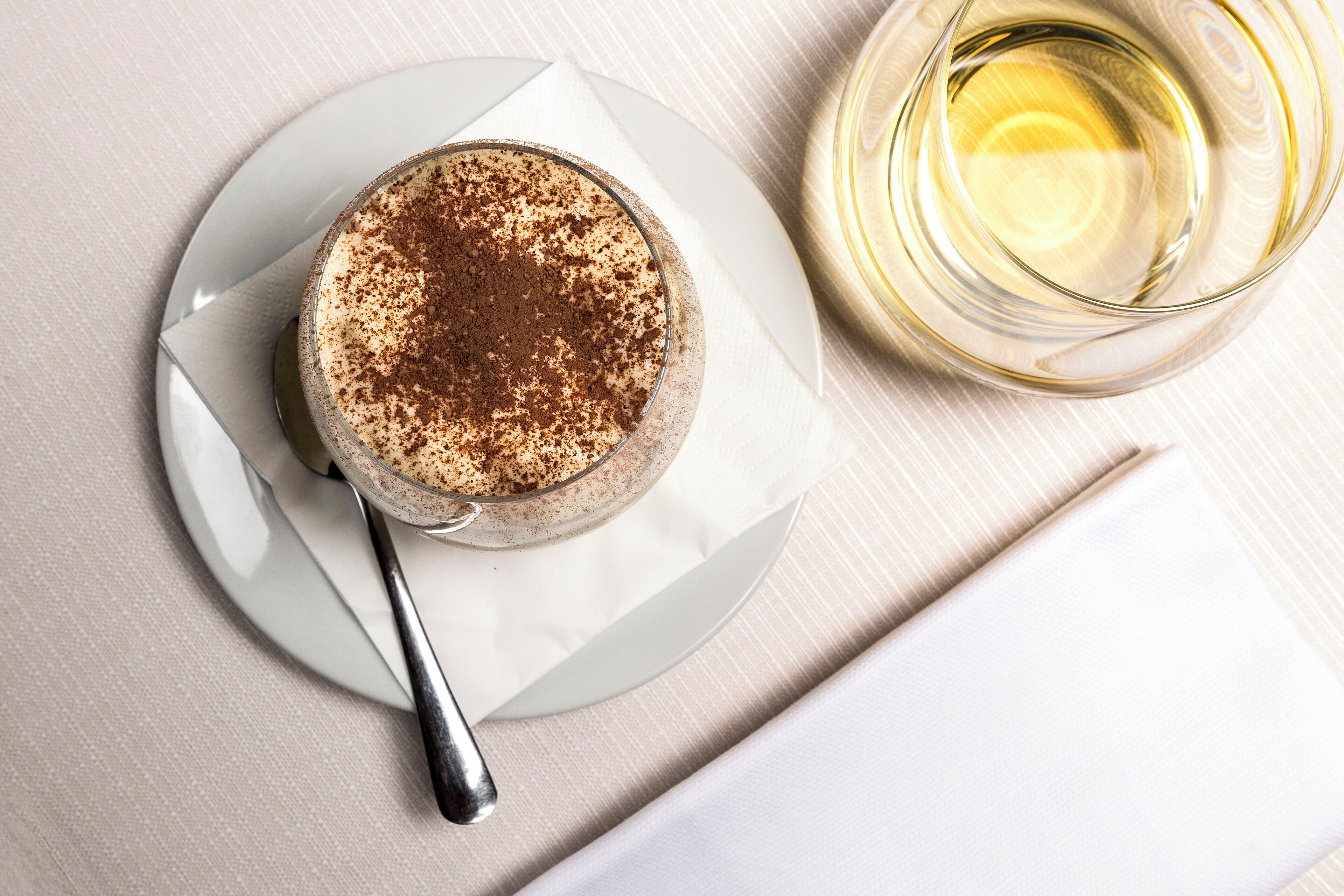 Dessert auf einem Teller mit einem Löffel, neben einem Glas Weißwein.