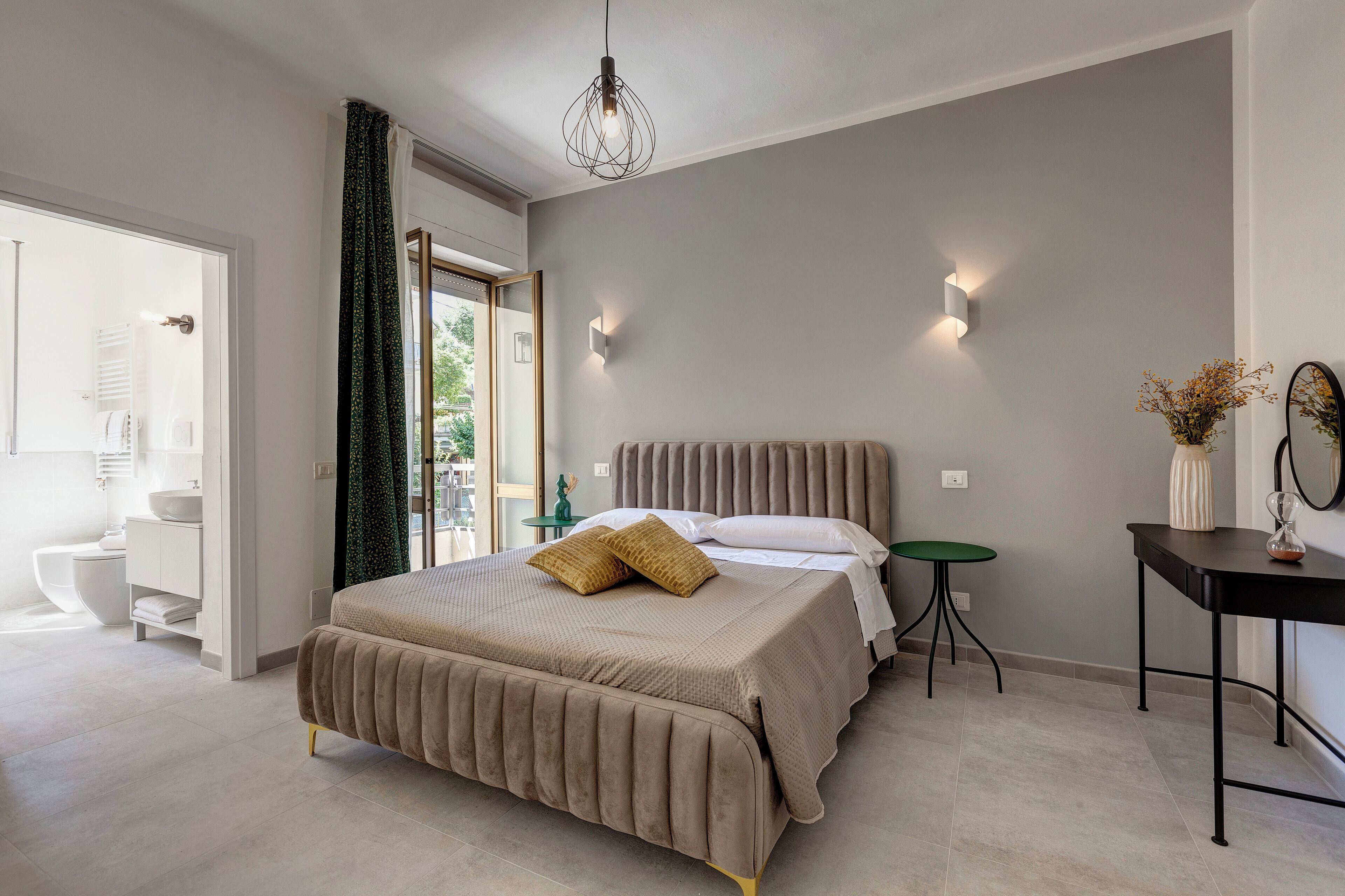 A modern bedroom with a large bed, a bedside table, a small green side table, and a mirror on the wall.