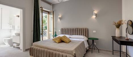 A modern bedroom with a large bed, a bedside table, a small green side table, and a mirror on the wall.