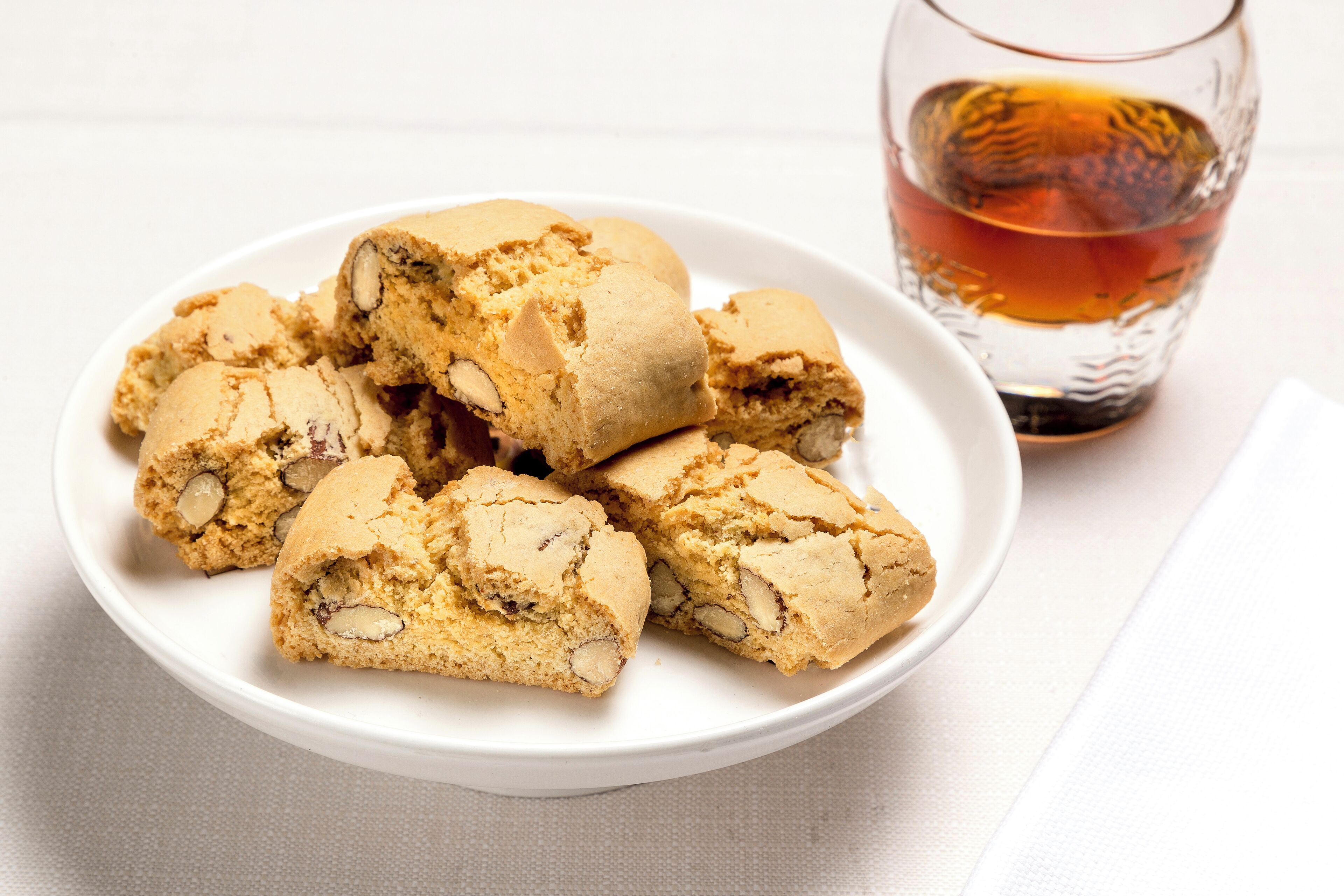 Un plato de galletas con nueces y un vaso de líquido ámbar.