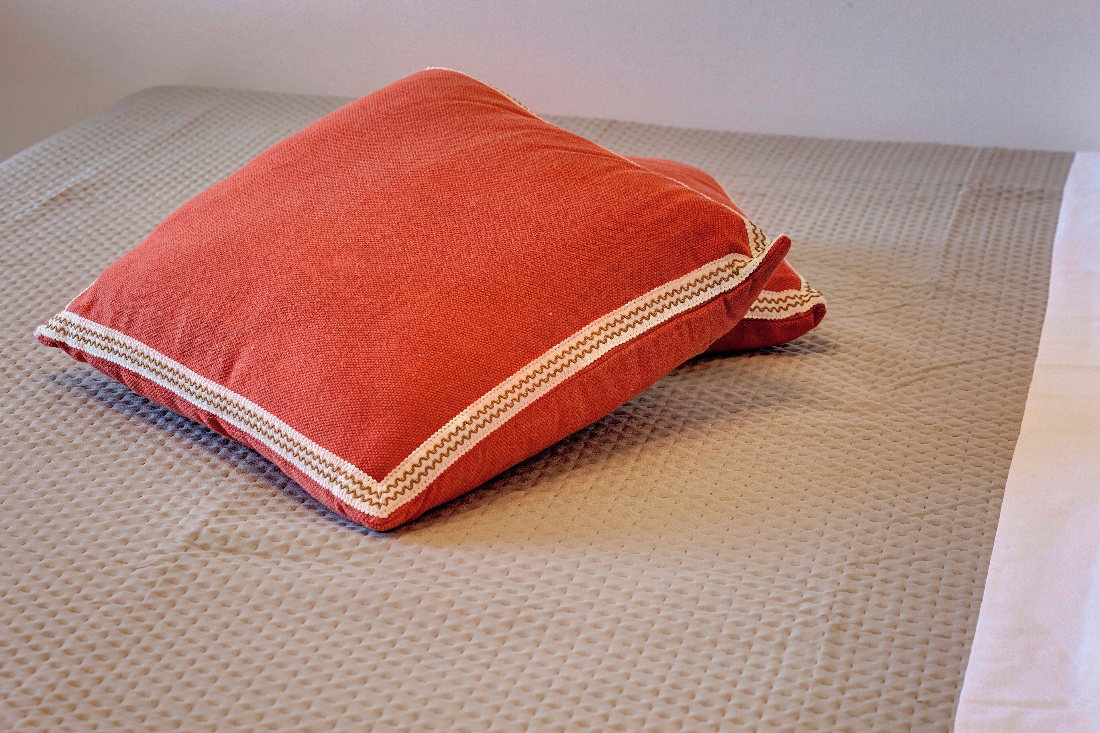 A red pillow with a white zigzag trim on a textured beige surface.
