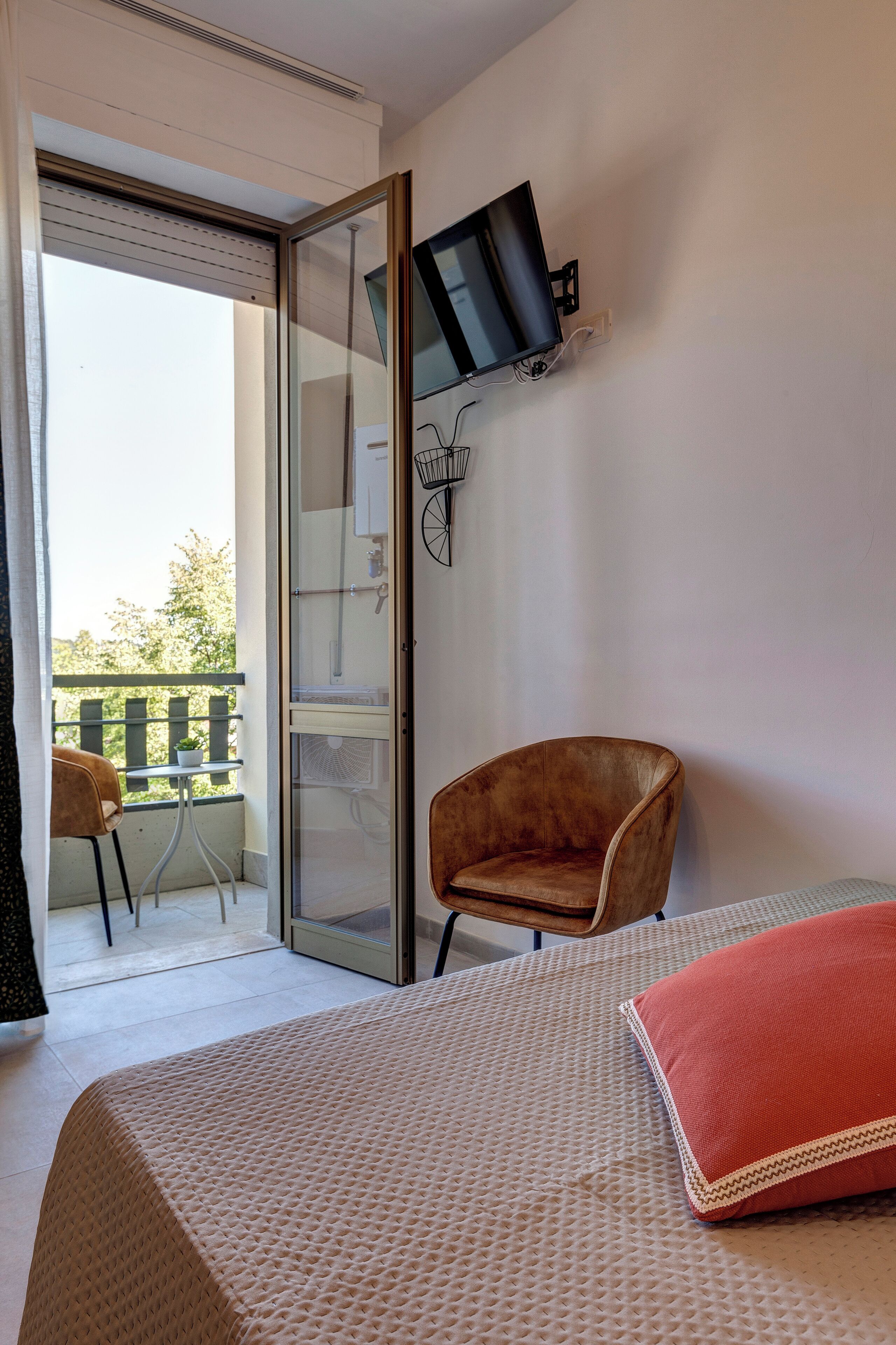 Une chambre à coucher comprenant un lit, un téléviseur fixé au mur, une chaise et un balcon avec une table et des chaises.