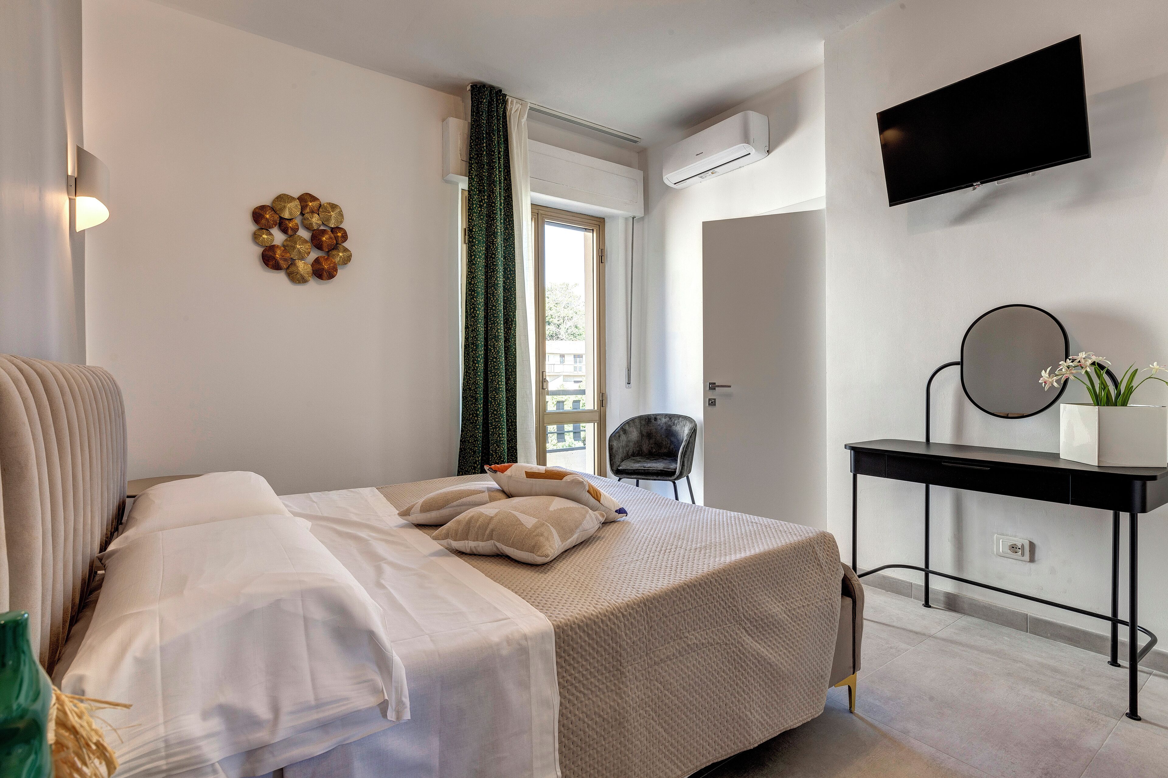 A modern hotel room with a bed, a desk, a chair, a TV, and a window with curtains.