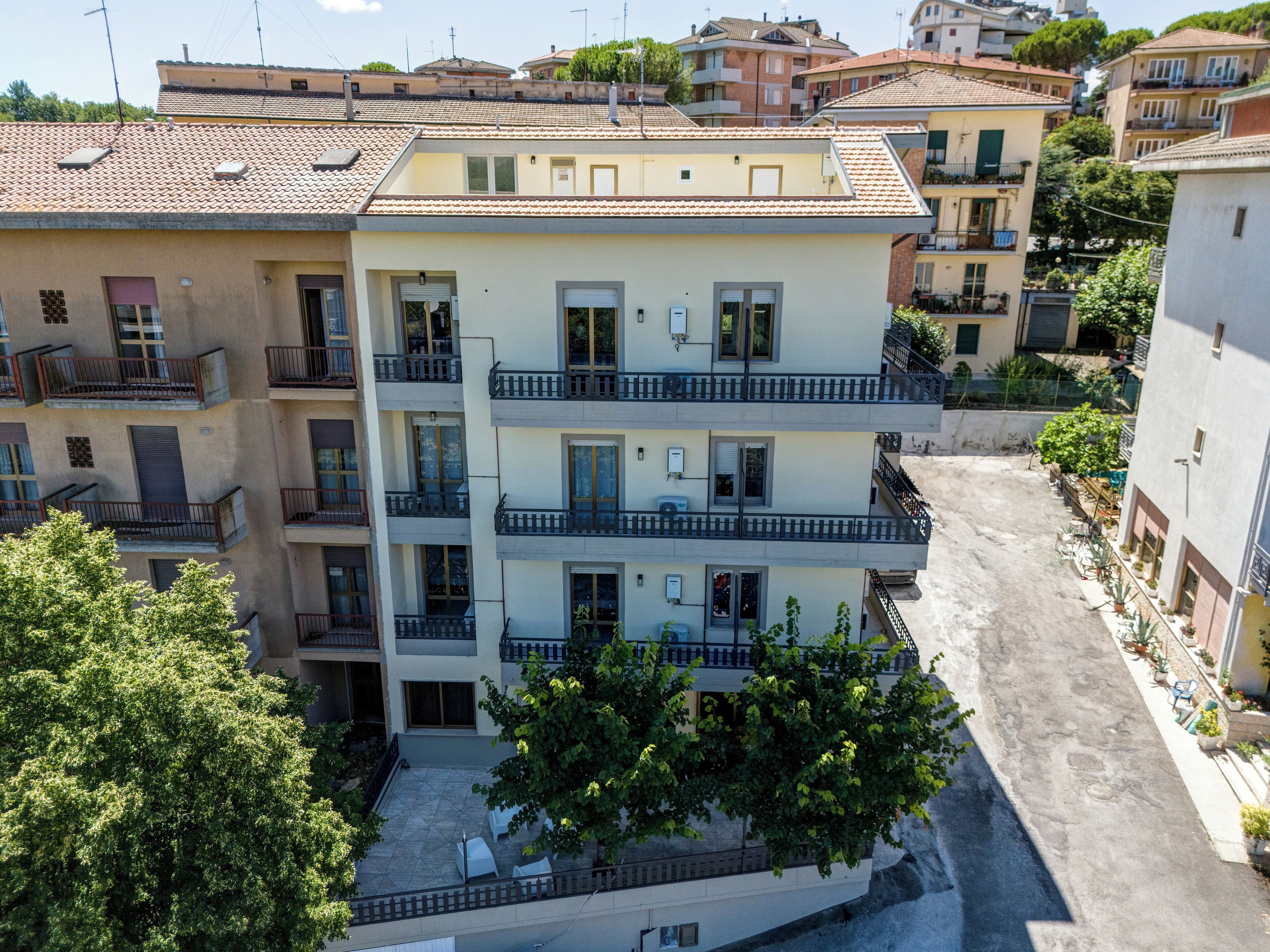 A multi-story residential building with balconies, a courtyard with outdoor seating, and a paved ground.