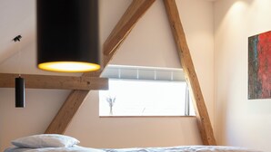 Un dormitorio con techo inclinado, una cama con ropa de cama estampada, una ventana con persianas y un cuadro en la pared.