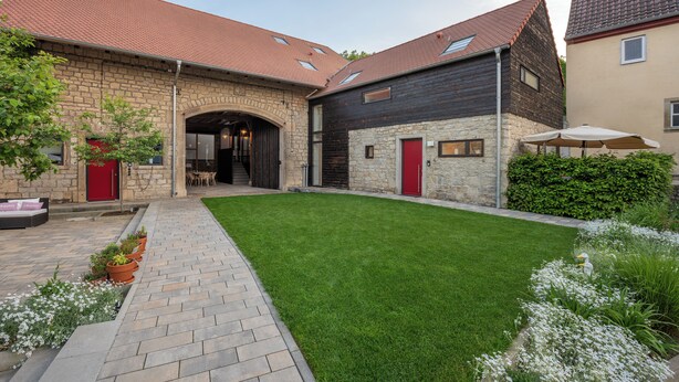 Un patio con un edificio de piedra, una estructura de madera y un césped bien cuidado.