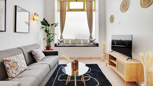 Un soggiorno moderno con un divano grigio, un tavolino in vetro, un mobile TV in legno e un'ampia finestra con tende.