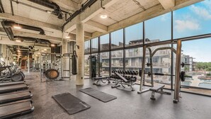 Una palestra con attrezzature per esercizi, ampie finestre e vista sugli edifici.