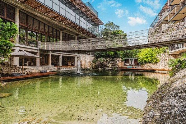 A modern building with a glass facade, a stone wall, and a bridge over a pond.