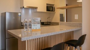 A modern kitchen with a granite countertop, stainless steel refrigerator, and black microwave. There are two black chairs and a sign on the counter. - w Cozy Bright 2BR Stay in Barranco (Lima)