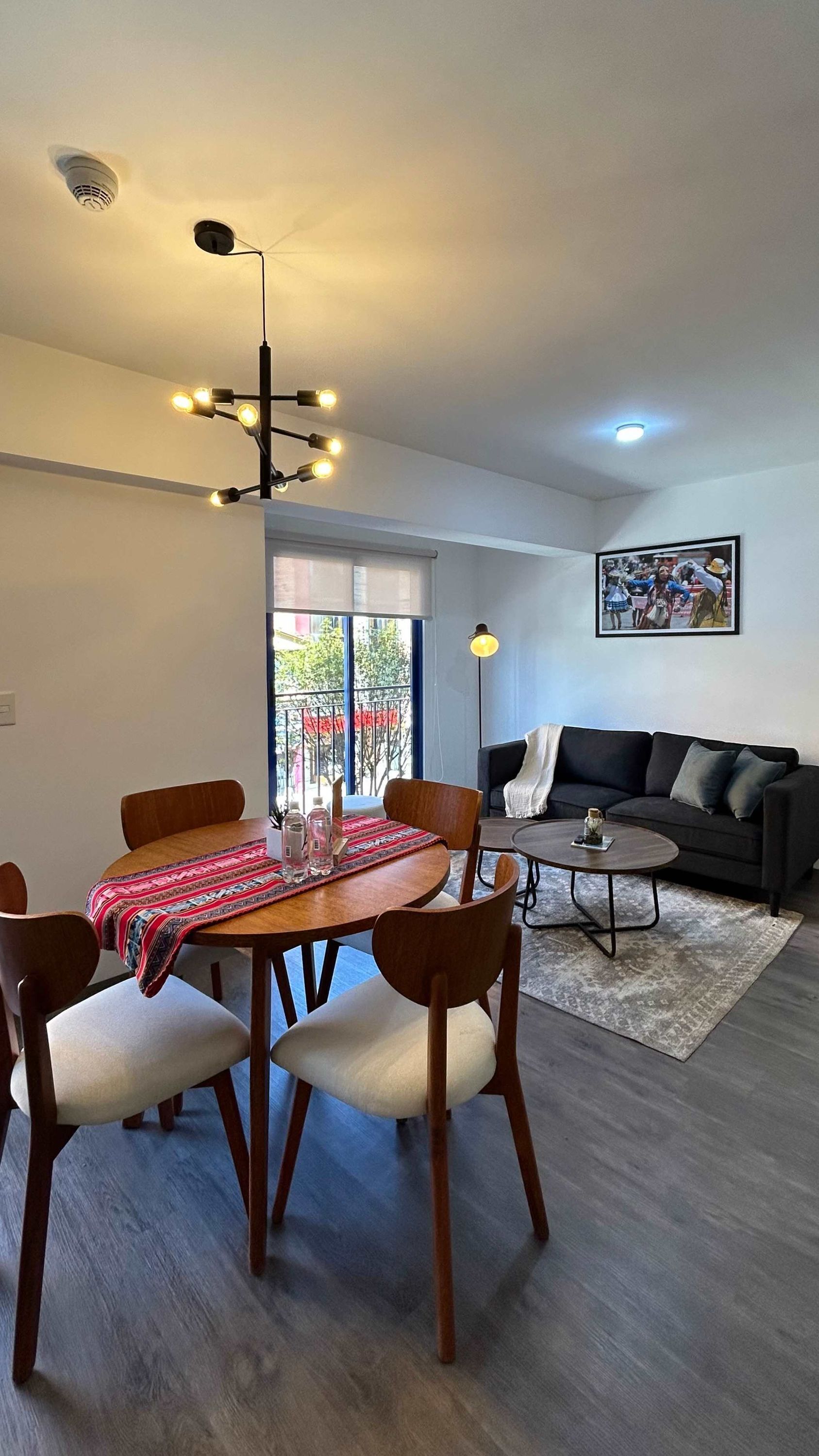 A dining area with a round table, chairs, and a chandelier. There is a sofa and a painting on the wall.