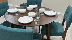 A dining area with a round table set for six, surrounded by teal chairs, a flat-screen TV mounted on the wall, and a wooden floor. - Mid-Century Modern Broad Ripple Stay with Style, Comfort & Local Color (Indianapolis)