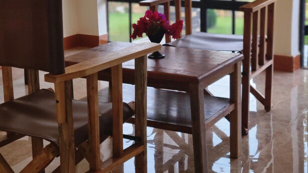 A dining area with wooden furniture and a large window with a view of greenery. - PUMZIKA HILL CAMPSITE (Kisongo)