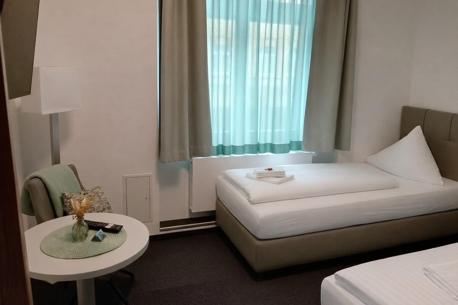 A hotel room with a bed, a desk with a lamp, a chair, and a window with curtains.