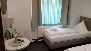A hotel room with a bed, a desk with a lamp, a chair, and a window with curtains.
