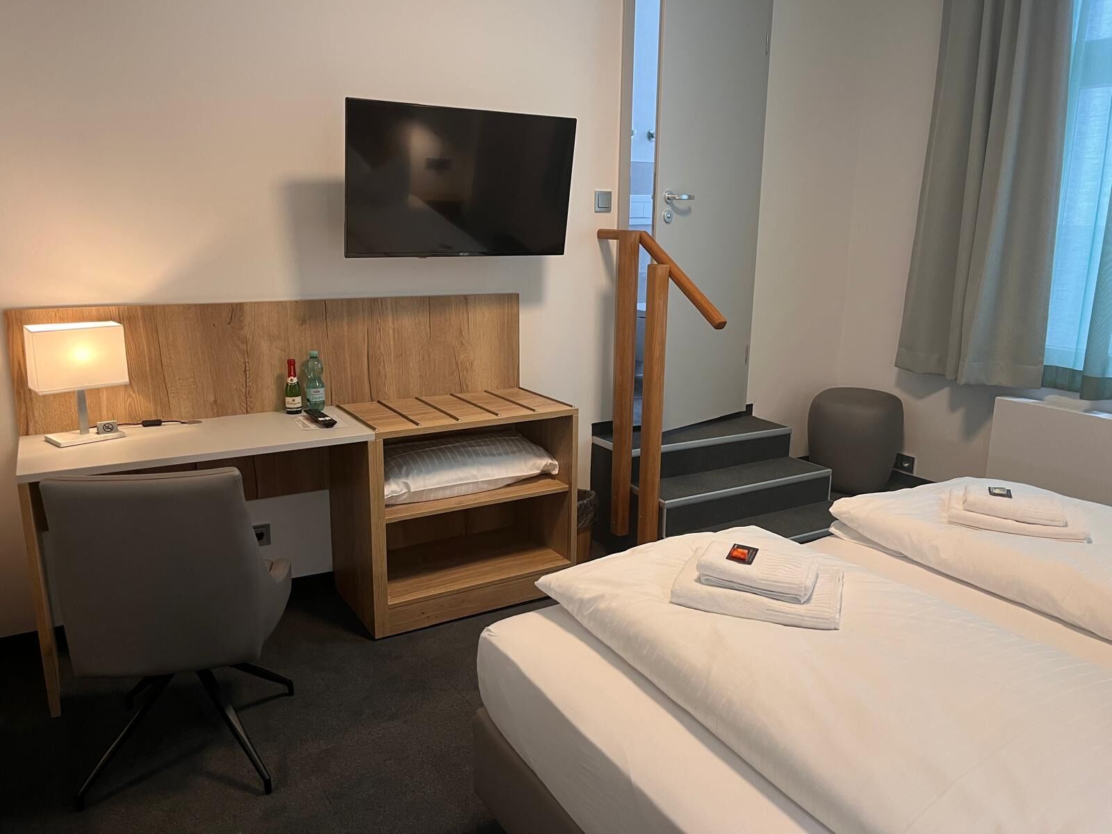 Habitación de hotel con escritorio, una silla, cama, televisor montado en la pared y una escalera.