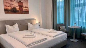 A hotel room with a large bed, two pillows, a small round table with a vase, and a chair.