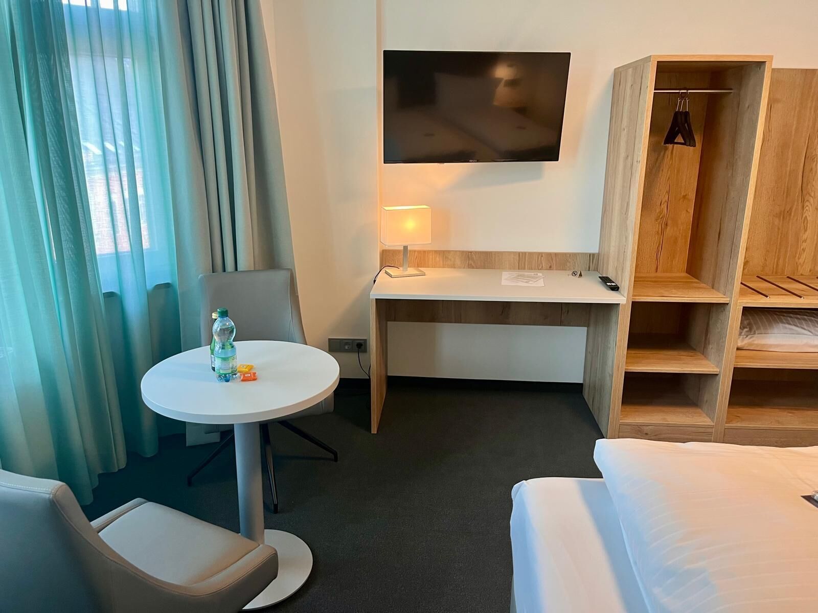 Habitación de hotel con cama, escritorio, silla, televisor y armario.