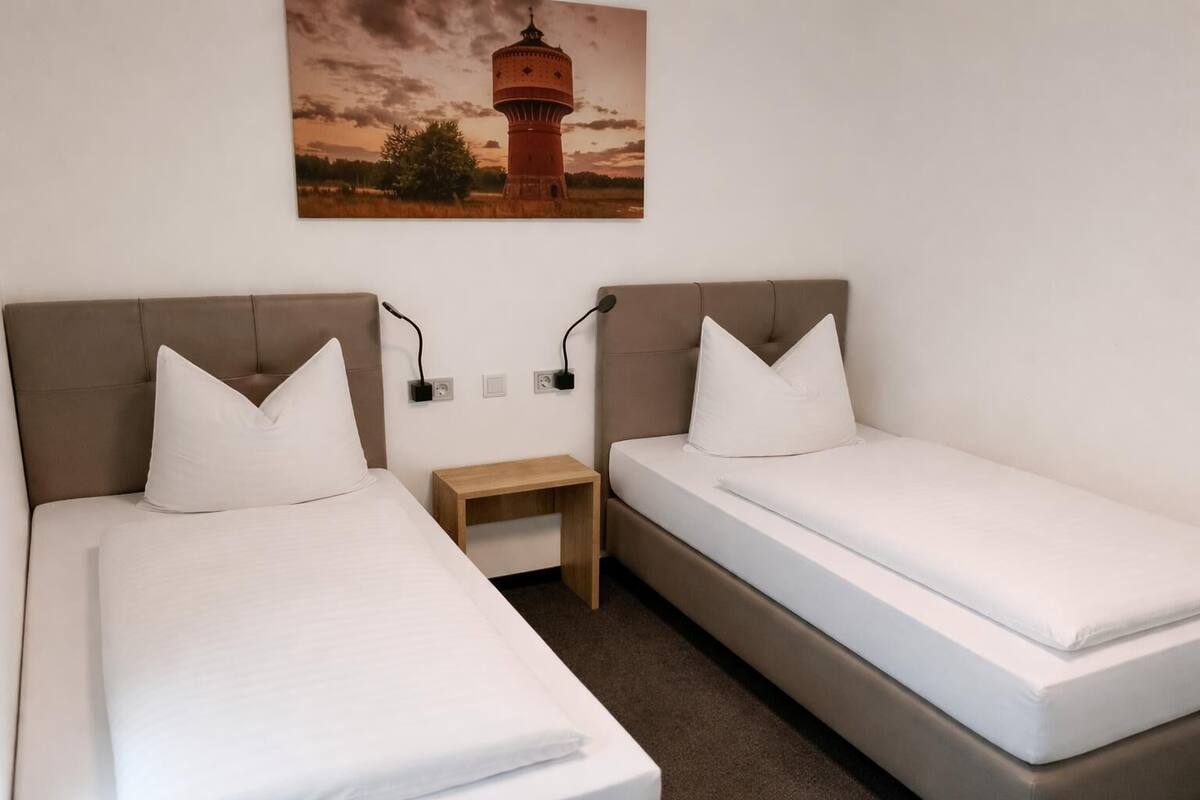 A twin room with two beds, a nightstand, and a painting of a lighthouse.